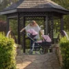 Daisy Chain Pinnacle Double Dolls Pram in Pink fabric for ages 6-13 years old. The pram has a silver frame with black accents. Cot has a black fabric body and pushchair seat has a black body. Both the cot and seat have hoods which are pink with a black and pink daisy that is removable. The cot has a pink apron. Photo shown is a girl leaning in to check on her doll.
