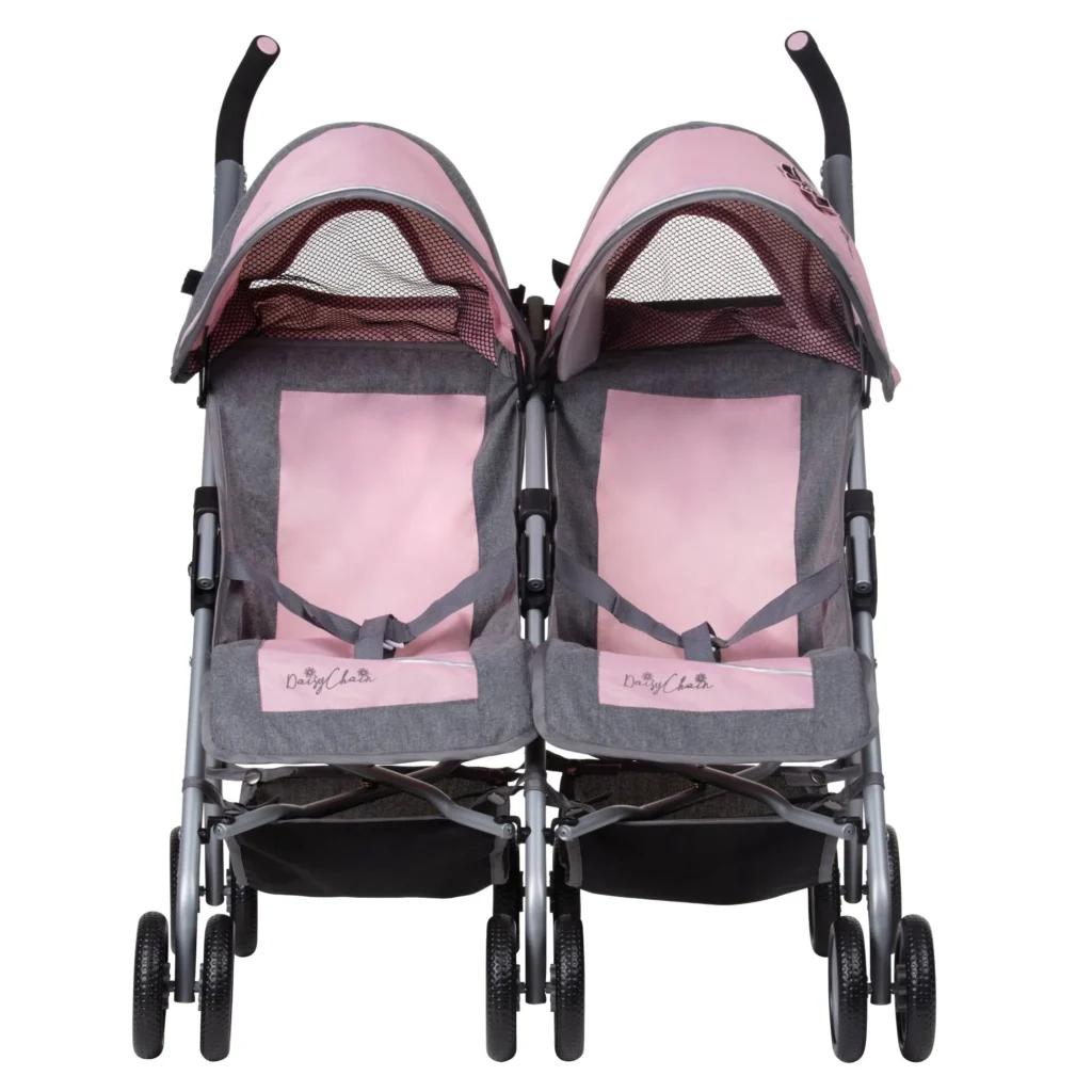 Daisy Chain Zipp Twin Max Dolls Pushchair in Classic Pink fabric. Shown front on. The pushchair has 2 seats side-by-side in the pink fabric with accents of grey and an embroidered Daisy Chain logo in silver. The pushchair has two hoods partly up and are mainly pink with accents of grey with a black and pink flower rosette. The wheels are black. The frame is silver and the two shopping baskets at bottom of the pushchair are black.