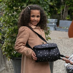an image of a girl with curly hair wearing a brown coat and holding a baby doll changing bag