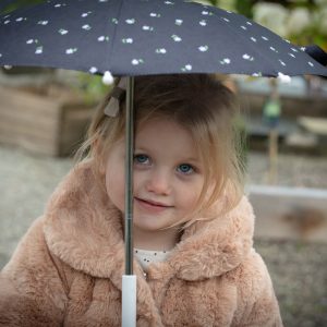a young girl stands under a black umbrella with white daisy pattern on it