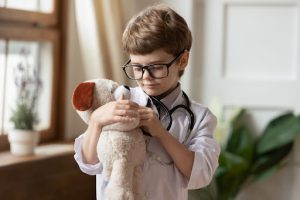 image shows a boy pretending hes a doctor with a teddy bear