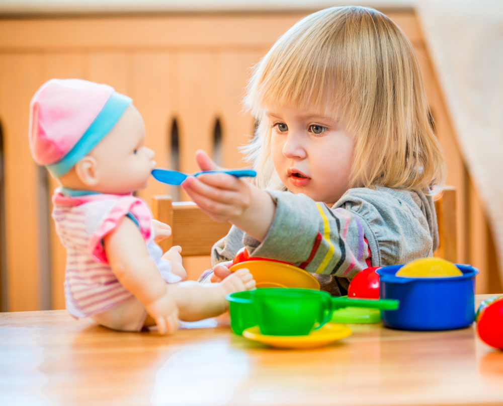 image of a blonde girl pretending to feed a baby doll