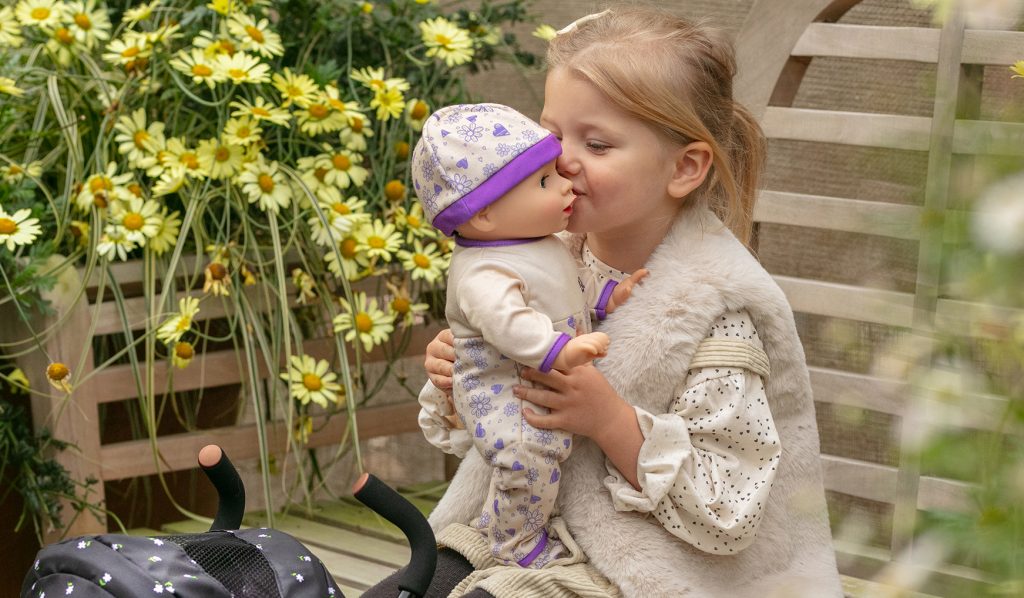 image shows a girl with blonde hair kissing her baby doll