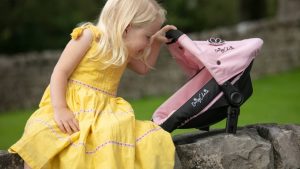 imagw shows a blonde girl playing with a pink dolls pushchair