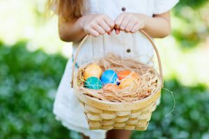 image shows a child holding a basket full of colourful easter eggs