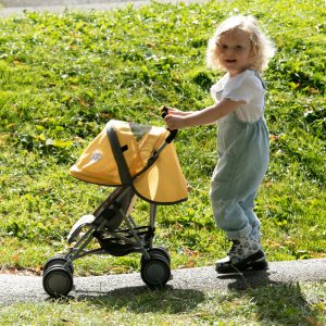 image of a girl playing outdoors with the daisy chain little zipp dolls pushchair in sunflower yellow