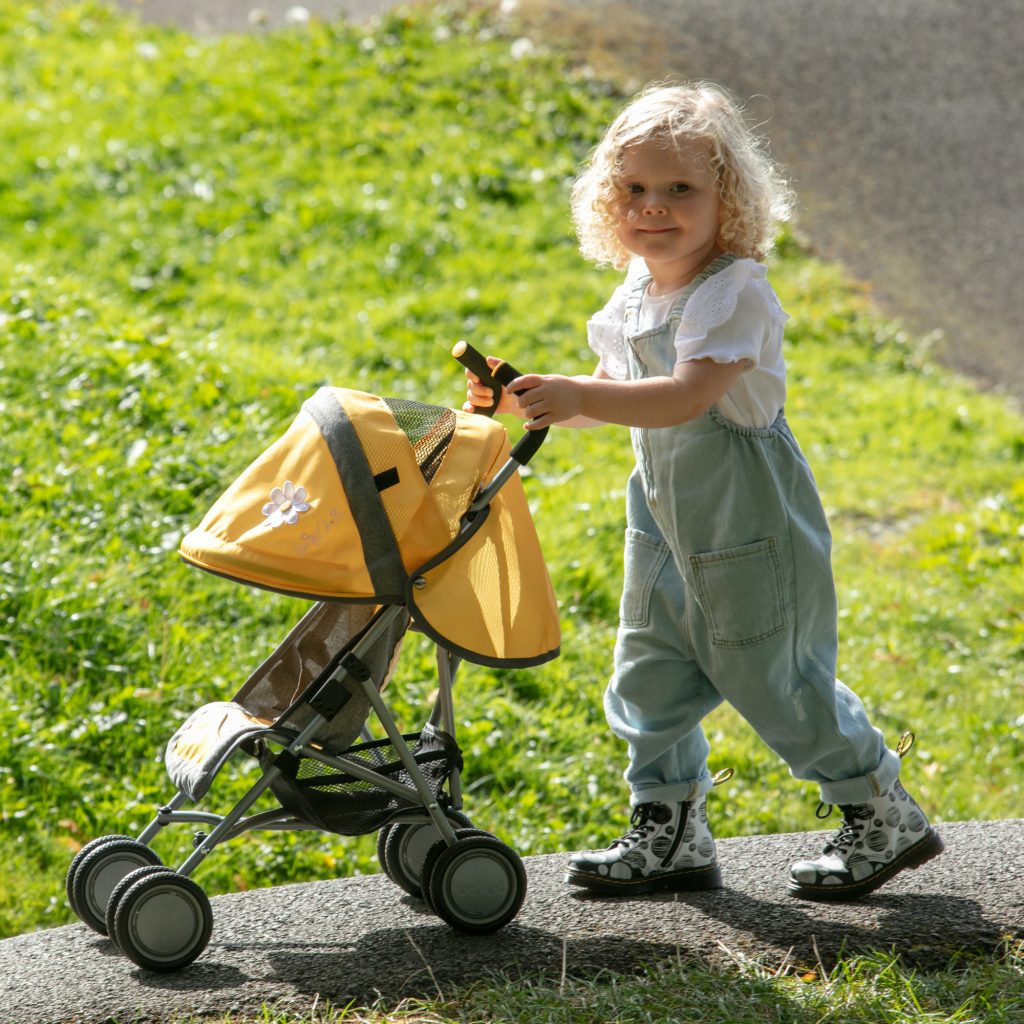 image of a girl playing outdoors with the daisy chain little zipp dolls pram