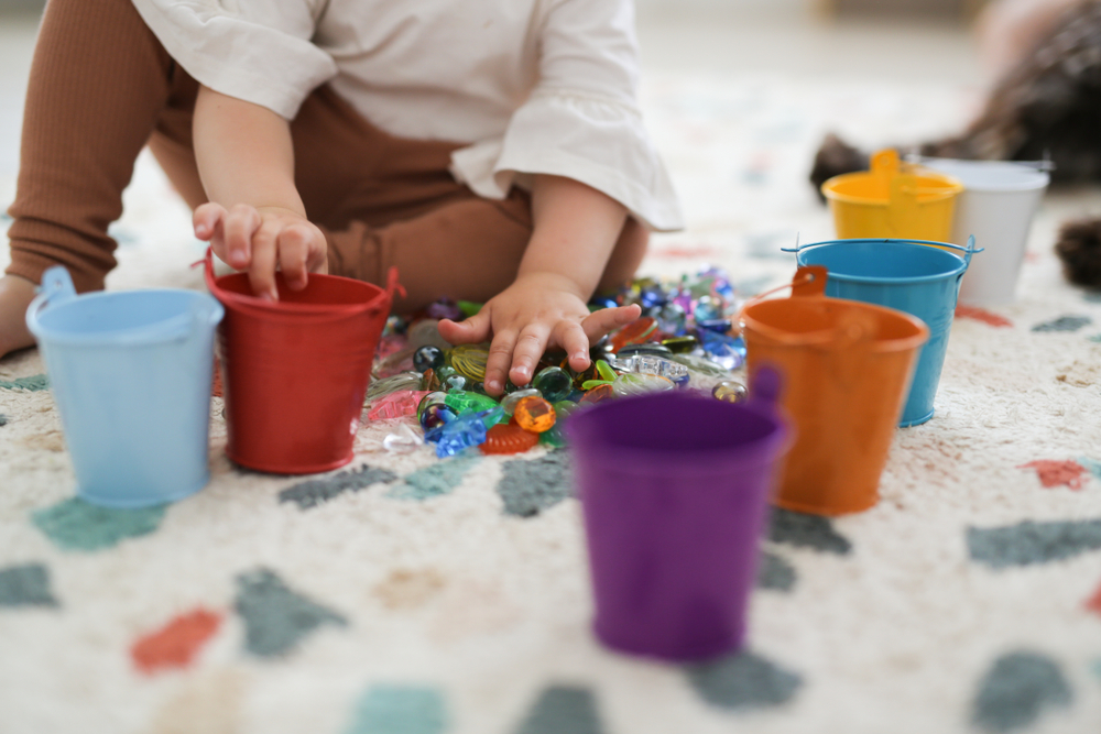 image of a toddler playing with lots of small objects and sorting them into coloured buckets