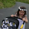 Girl wearing a daisy headband is pushing the Daisy Chain Connect dolls pram. Handle and hood of the pram only visible. Hood shows the bumblebee fabric of the dolls pram.