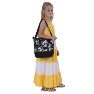Daisy Chain Luxury Tote Bag in Bumblebee fabric . Bag has carry handles and black shoulder strap. Bag is in bumblebee fabric with a black leatherette band around the bottom of the bag. Girl with blonde hair and wearing a white and yellow striped summer dress is holding the bag by the shoulder strap.