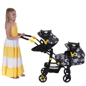 Daisy Chain Pinnacle Double Dolls Pram in Bumblebee fabric. The pram has a black frame with yellow accents. Cot has a bumblebee fabric body and pushchair seat has a black body. Both the cot and seat have hoods which are half black and half bumblebee fabric. Girl with long blonde hair holding pram handles on left of shot in a yellow and white striped summer dress.