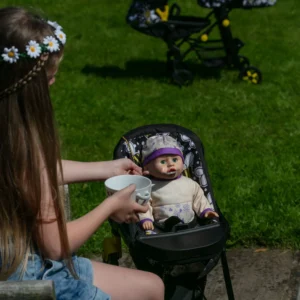 Girl with long brown hair is feeding her doll which is sat in the Daisy Chain High Chain in bumblebee fabric.