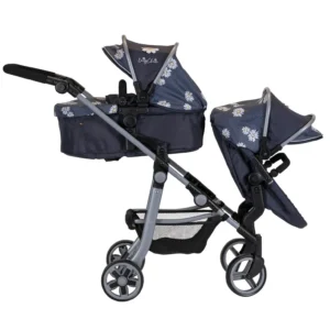 Daisy Chain Pinnacle Double Dolls Pram in Daisy Dot fabric for ages 6-13 years old. Hood is up and is mainly navy blue with accents of daisy's and white polka dots Silver metal with a white and yellow flower rosette and an with an embroidered Daisy Chain logo in white. There is a cot on the top part of the pram facing the handle and a pushchair seat on the bottom facing outwards away from the handle. Wheels are black and Silver with a shopping basket at bottom of pushchair which is black. The frame of the pushchair is silver
