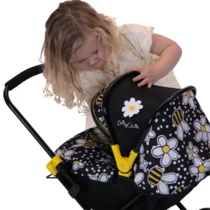 Daisy Chain Pocket Pram in Bumblebee - For ages 18 months - 3 years. Black frame with yellow accents, black cot and Bumblebee fabric hood. Girl stood behind in a summer dress.