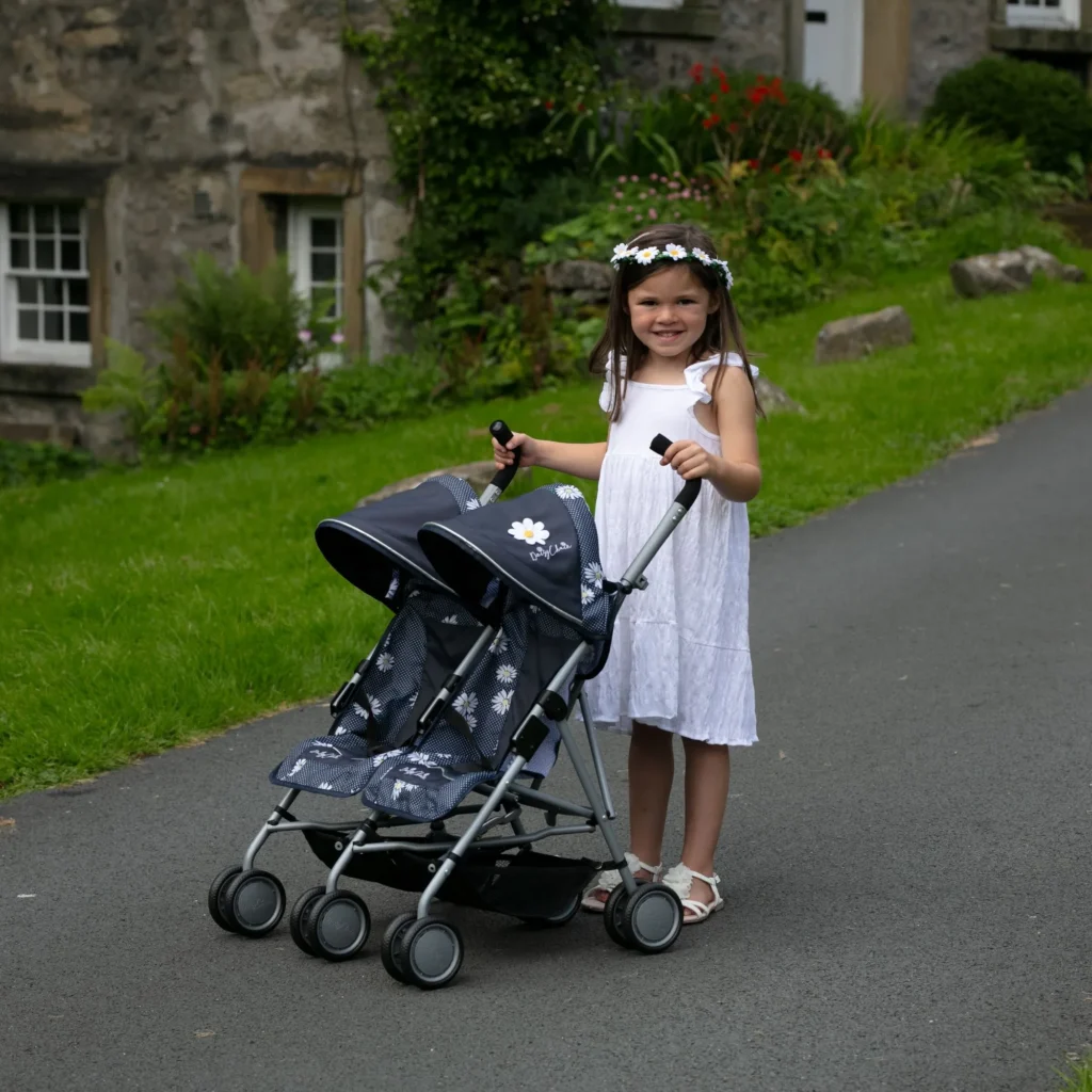 image of a girl in a white dress playign with a double dolls pushchair outdoors